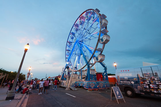 Ferris Wheel on street lit up in the evening with blue sky in the background